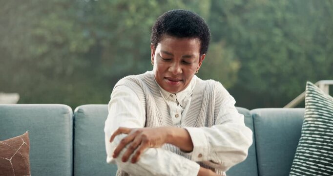Black woman, massage and discomfort on sofa with elbow pain, inflammation and symptoms of arthritis. Mature person, stretching and injury at house with muscle gout, rheumatic disease and osteoporosis