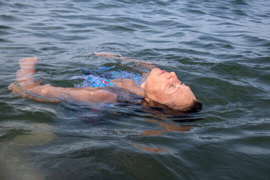 Donna anziana che galleggia a dorso sul pelo dell'acqua calma del lago nel Parco del Gelso a Bellaria Igea Marina, momento di relax e benessere a contatto con la natura