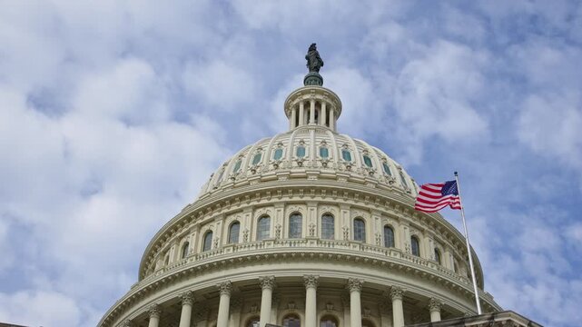 American flag displayed on Capitol. American flag set against clouds over US Capitol. American flag bold symbol of Amerika democracy. American flag on famous Capitol dome in Washington DC.