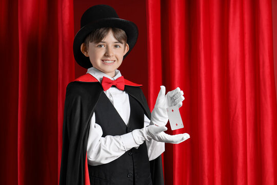 Little magician with levitating playing card against red curtains