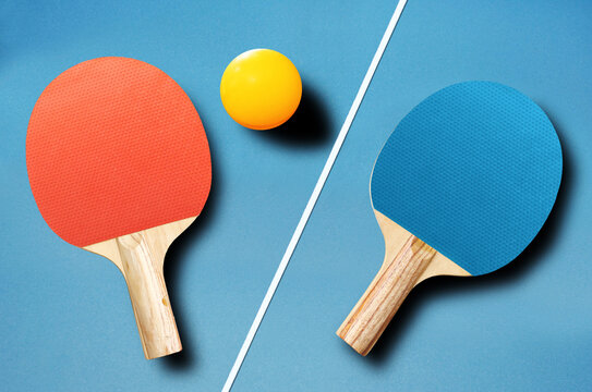 Pin pong ball with red and blue paddle on blue board