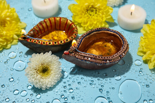 Diya lamps with candles and chrysanthemum flowers in water on blue background. Divaly celebration
