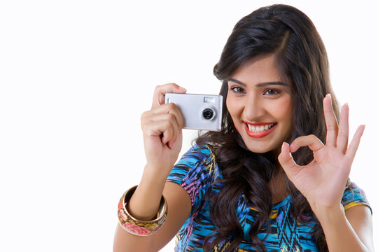 Young woman taking photograph with camera and showing OK sign