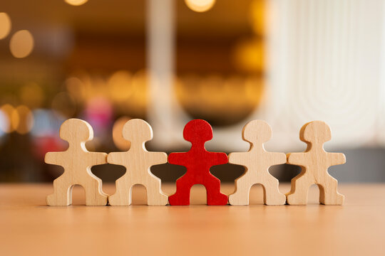 Red wooden figure standing out in a row of standard wooden figures. Ideal for individuality, leadership, talent recruitment, uniqueness, and standing out commercial business concepts.
