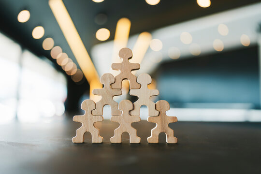 Stack of wooden human figures forming a solid pyramid on dark table. Ideal for corporate teamwork, business organization hierarchy, leadership, and human resources commercial concepts.