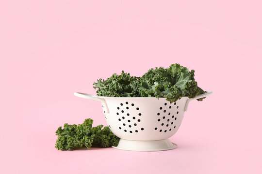Colander with fresh leaves of kale cabbage on pink background