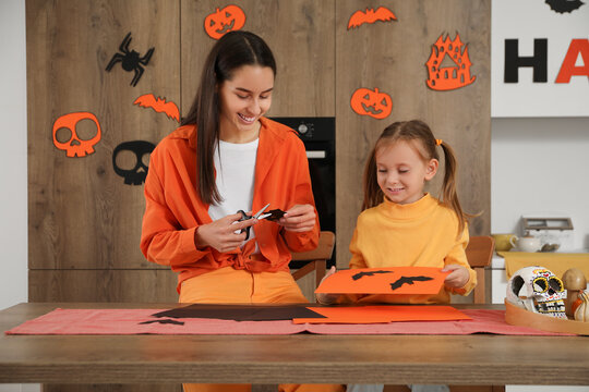 Little girl with her mother making Halloween decorations at table in kitchen