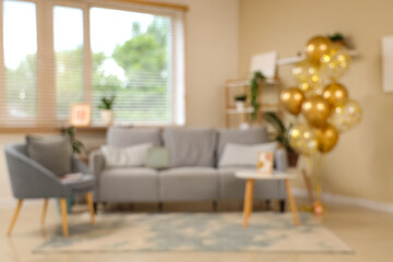 Obraz premium Beautiful golden air balloons with sofa and armchair near beige wall at home, blurred view