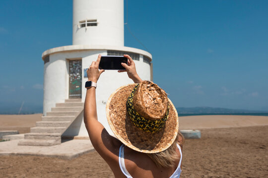 Woman takes phone photo of a beach lighthouse
