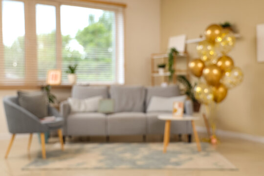 Beautiful golden air balloons with sofa and armchair near beige wall at home, blurred view