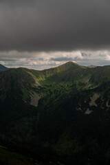 Sunlight illuminates a green mountain under storm clouds © Cavan