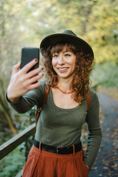 Smiling woman in a hat takes a selfie, autumn city park