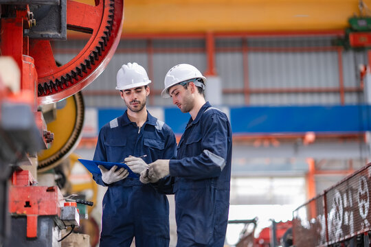 Factory engineers review inspection checklist, inspect production machine, discuss maintenance process, support quality control, equipment reliability, manufacturing operation, factory safety.