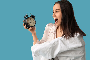 Pretty young woman with blanket and alarm clock on blue background