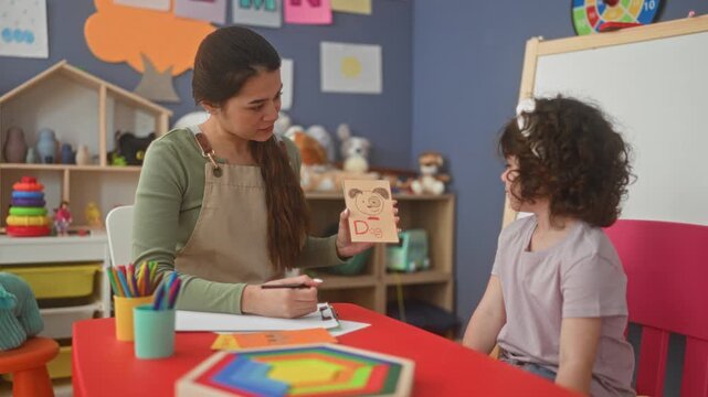 Teacher holds pink flashcard with cat and points finger to child in school building; early literacy joy.