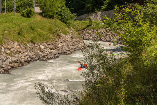 Dynamic outdoor sports image featuring a kayakers navigating swift rapids on a crystal-grey glacial river in the Swiss mountains.