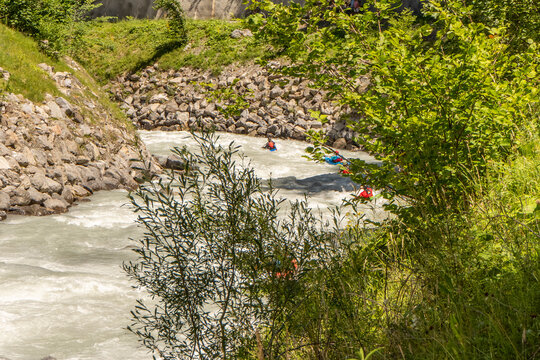 Adventure travel photograph of whitewater kayaking on a rushing alpine river with turbulent water and rocky riverbanks in Switzerland.