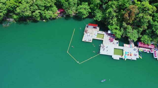 Scenic aerial view of a floating recreational platform on Dayang Bunting Lake featuring emerald freshwater, tropical rainforest, and visitors enjoying outdoor activities.