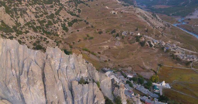Annapurna Circuit, Manang Nepal, orbit drone shot of ancient Bhraka Monastery perched on rocky mountain cliffs above Marsyangdi River valley.