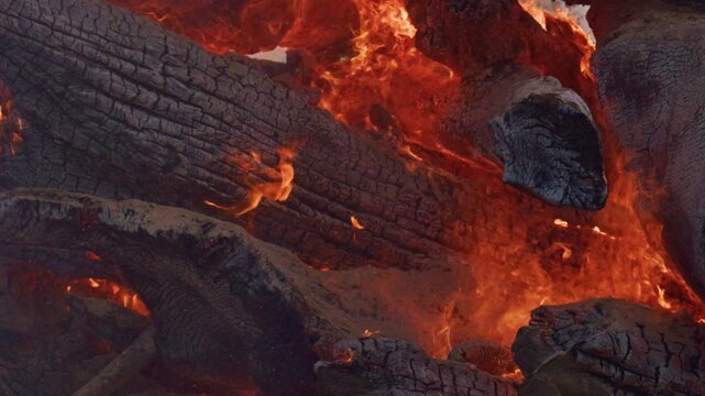 Burning Firewood Logs with Intense Flames and Glowing Embers Close Up, Extreme burning firewood logs with flames, glowing embers, blackened charcoal, and intense heat.