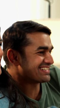 ndian Asian young friends, a boy and a girl in their twenties, sitting on a cozy sofa at home, playing a video game with joysticks, enjoying fun moments, laughing, competing, and bonding together