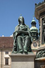 Fototapeta premium Statua allegorica della Pietà nel monumento a Francesco I con la torre dell'orologio dell'Amalienburg sullo sfondo alla Hofburg di Vienna, Austria