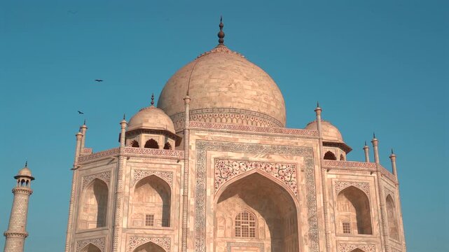 A low-angle view highlights the iconic main dome, ornate archways, and detailed marble inlay of the Taj Mahal in Agra.