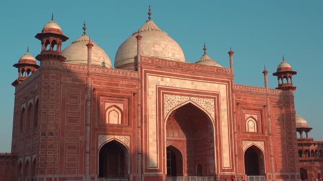 Warm sunlight illuminates the red sandstone facade, white marble domes, and arched entrances of the mosque at the Taj Mahal complex in Agra.