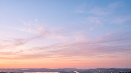Fototapeta premium Pastel sunset sky with soft clouds over a distant rural landscape at dusk