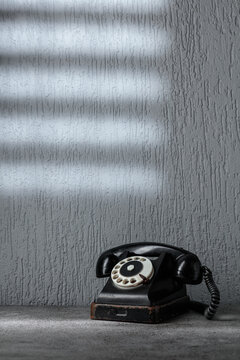 Vintage black telephone with rotary dial on gray stone table.