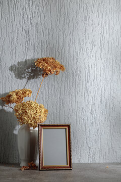 Empty picture frame and white vase with dry flowers on a background of gray wall.