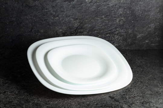 Empty white plates on a black stone background with copy space.