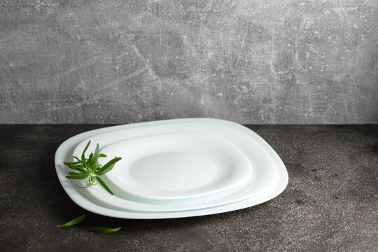 Empty white plates with rosemary on a grey stone background.