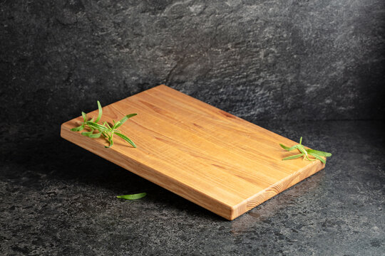 Empty cutting board with rosemary on a black stone background.