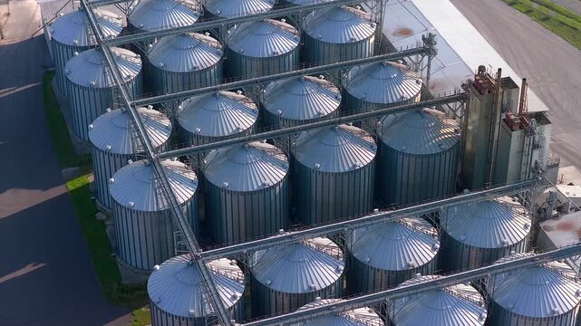 Large metal grain bins at a modern agricultural complex for storing cereal crops. Aerial orbiting view of the agro industrial elevator