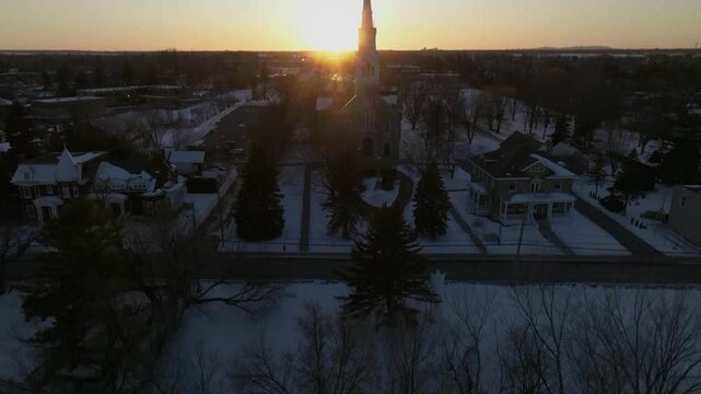 drone asending overlooking the bigest church in chambly quebec canada in the winter sun in the back cementery n coastline