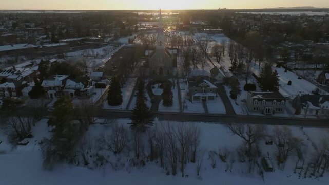 drone approaching the bigest church in chambly quebec canada from the river to the main entry exposing the cementery in the back
