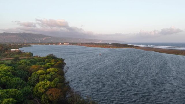 Aerial view of the afternoon landscape of the downstream of the Opak River, with boats visible, the Kretek Dua Bridge and the hills of Bantul, Indonesia in the background.