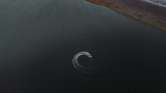 Aerial view of jetski making circular pattern during sunset and looks darker in lagoon or baros beach bantul indonesia.