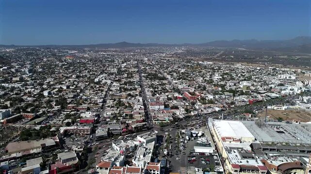 Static drone shot panning over the town of Cabo San Lucas, Baja California Sur, overlooking the landscape with a glimpse of Puerto Paraiso Mall and Cerro Colorado hill in the distance.