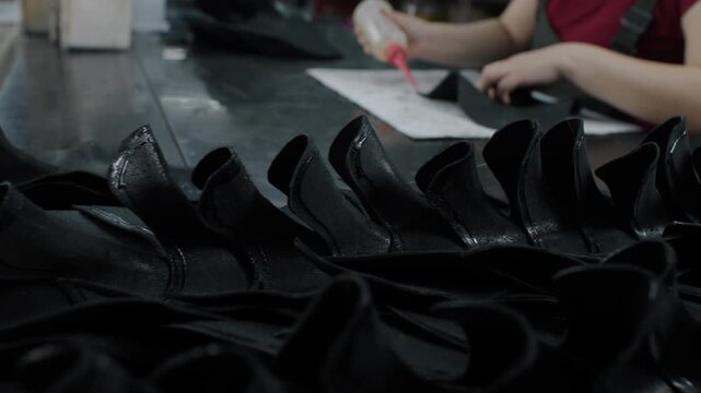 Worker assembling black shoe uppers by hand at a factory workbench indoors