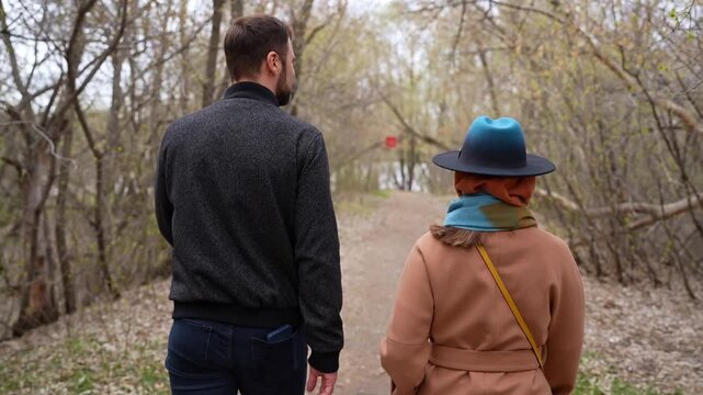 Happy couple walking throught autumn park together, holding hands and smiling in coats. Woman in camel coat and bright hat
