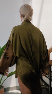 Elegant woman wearing luxury kimono robe in modern tropical home.