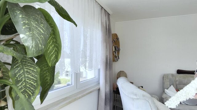 A woman cleans a living room window using a professional window cleaning tool with a telescopic handle and microfiber pad.