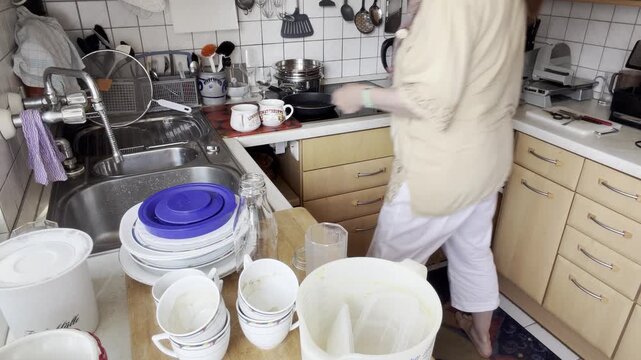 Barefoot woman organizes dishes, glasses and kitchen utensils at the sink before washing in a clean home kitchen.