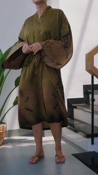 Elegant woman wearing luxury kimono robe in modern tropical home.