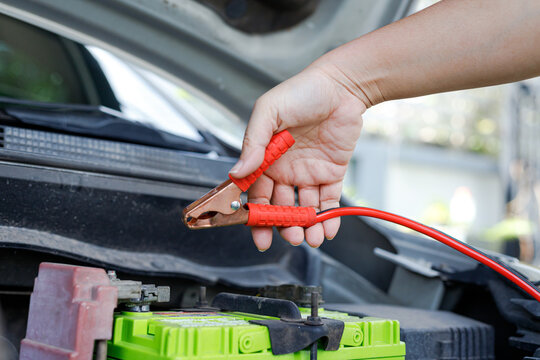 Hand holding jumper cable clamp near car battery