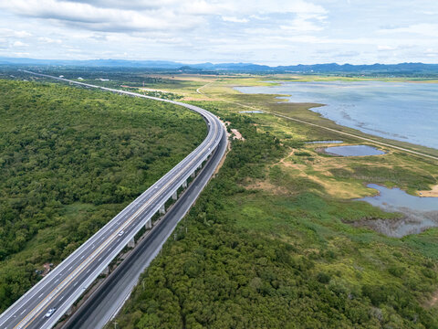 Drone aerial view of an elevated highway crossing lush forest and mountain landscape under dramatic clouds, The modern transportation infrastructure and nature concept