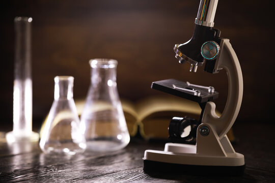 Vintage Laboratory Equipment: Microscope and Glassware on Wooden Table with Open Book in Background