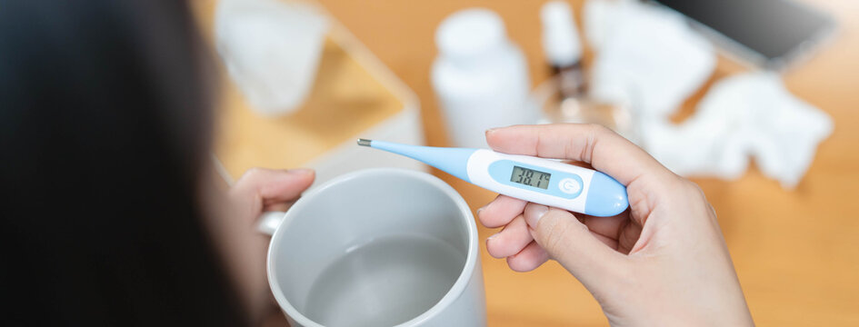 Sick person resting in bed checking temperature with thermometer, suffering from high fever, seasonal flu, influenza virus infection, and common cold symptoms at home